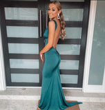 Woman in a teal evening gown with an open back standing in front of a modern glass door.