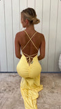 Person wearing a yellow dress with criss-cross straps in front of a white wall.