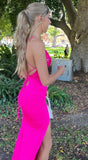 Woman in a bright pink dress standing outdoors near trees and a building.