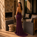 Woman in a purple evening gown standing in a sunlit room with stone walls and furniture.