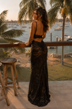 Woman in a black lace dress standing on a balcony overlooking a waterfront with palm trees.