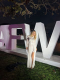 Person in a white dress standing next to a large letter 'W' at night.