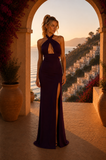 Woman in a black evening gown standing in an archway with a scenic view of a coastal town.
