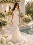 Woman in a white lace wedding dress standing in a decorated outdoor setting with flowers and columns.