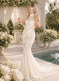 Woman in a white lace wedding dress standing in a decorated outdoor setting with flowers and columns.