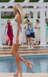 blonde model wearing I Am Woman Mini dress by Amy Taylor Collection next to pool. view from left hand side